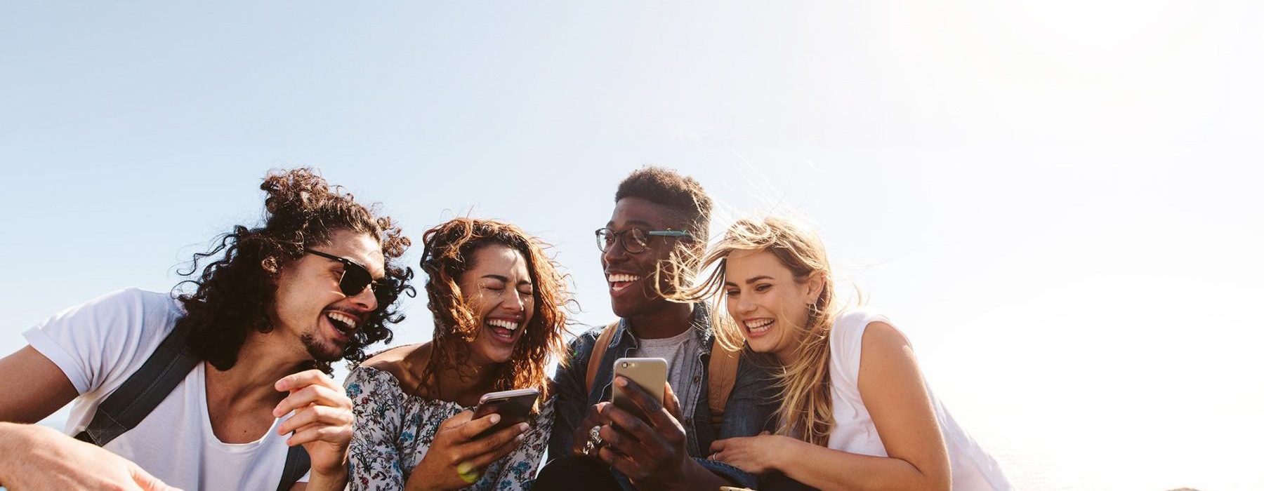 a group of friends sit outside laughing over their cell phones